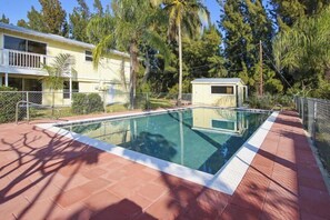 Une piscine rectangulaire, bordée d’une terrasse carrelée et entourée d’une clôture et d’arbres.