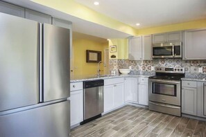 Une cuisine moderne dotée d’appareils électroménagers en acier inoxydable, de meubles blancs et de carreaux décoratifs sur le mur derrière l’évier.