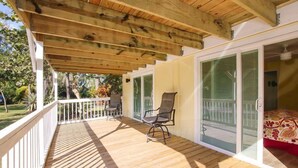 A covered outdoor deck with wooden flooring, a white railing, and two chairs. - Pine Island Tropical Retreat 1 (Saint James City)