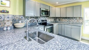 A kitchen with grey cabinets, a stainless steel sink, a microwave, and a patterned backsplash. - Pine Island Tropical Retreat 1 (Saint James City)