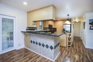 A modern kitchen with a central island, wooden cabinets, and a view to a patio. - Pine Island Linas Tropical Retreat (Saint James City)