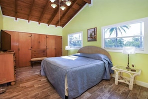 A bedroom with a bed, wooden wardrobe, bench, and two windows.