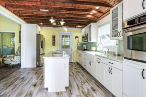 A kitchen with white cabinets, a central island, a wooden ceiling, and a door leading to another room.