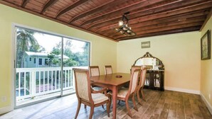 Comedor con mesa y sillas de madera, una araña y vistas a una casa a través de puertas correderas de vidrio.