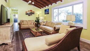 Una sala de estar con techo de madera, un sofá color crema, una mesa de centro y un ventanal con vistas a árboles.