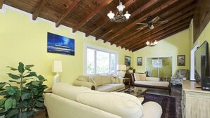 Un salón amplio con techo alto, un ventanal grande y un televisor sobre un mueble de madera.