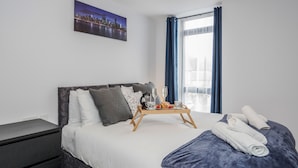A neatly made bed with a tray of breakfast items, a blue blanket, and towels on the side. - Watford Cassio Deluxe - Modernview Serviced Accommodation (Watford)