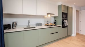 A modern kitchen with a built-in oven, a sink, and a countertop with a kettle and a toaster. - Watford Cassio Deluxe - Modernview Serviced Accommodation (Watford)