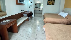 A hotel room with a bed, a desk, a chair, a TV, and a bathroom in the background.