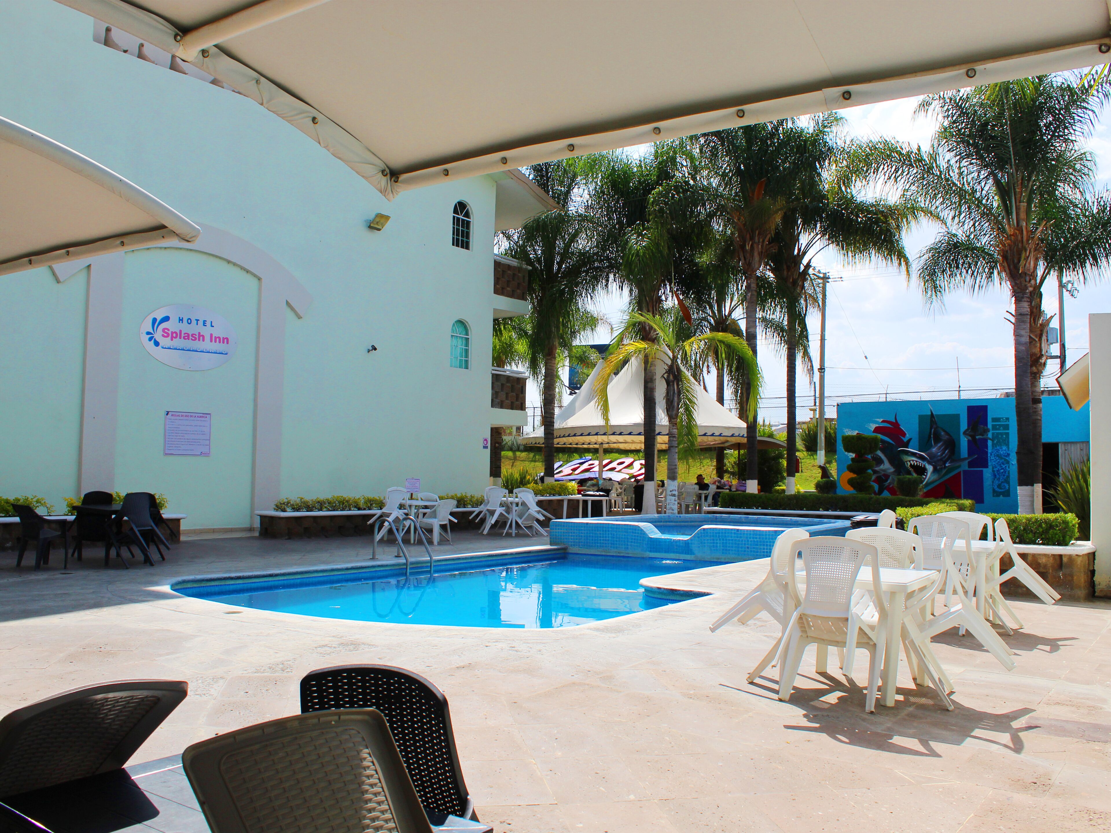 A hotel pool area with lounge chairs, a sign for 'Hotel Splash Inn,' and a mural on the building.