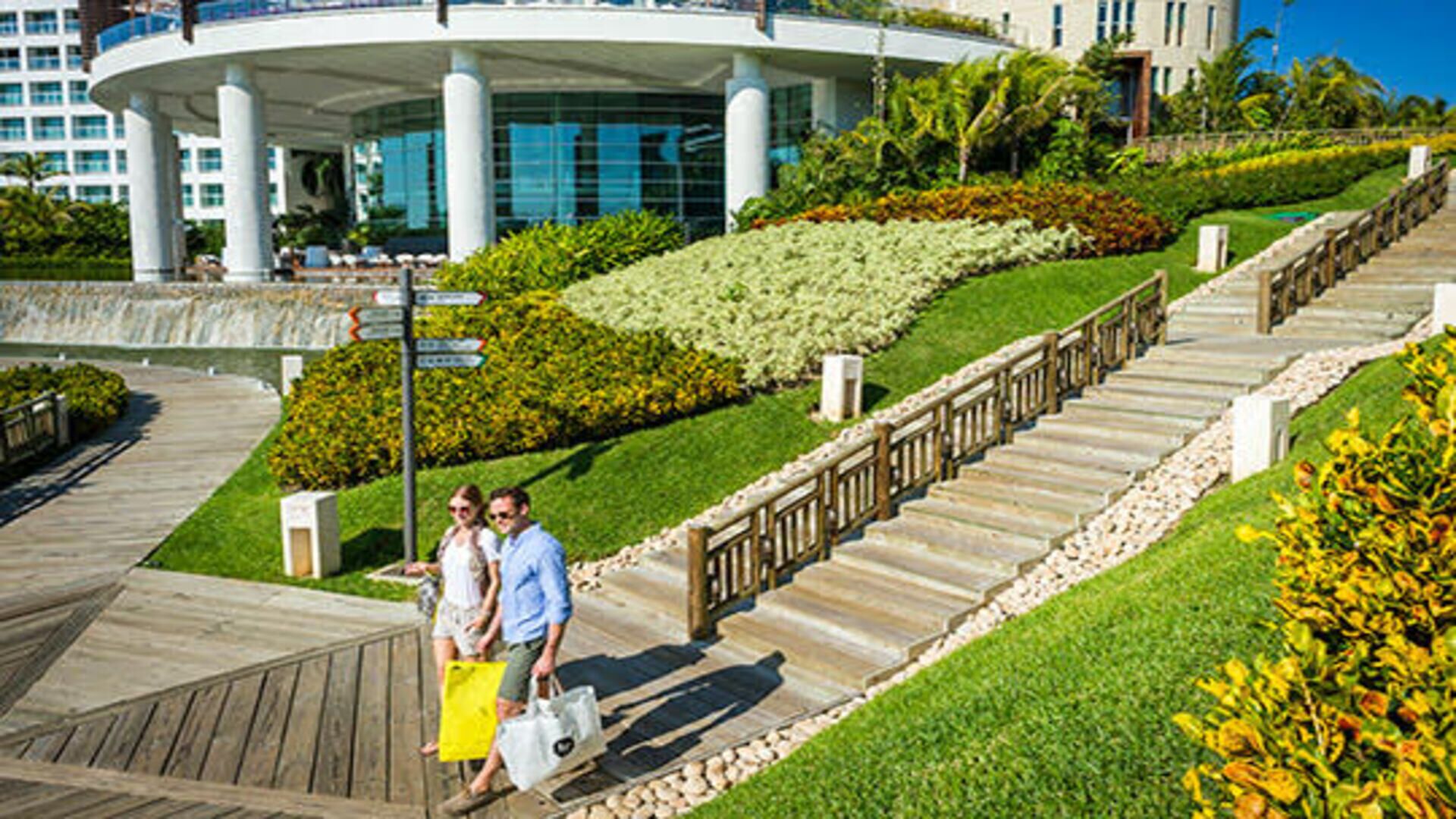 Ein modernes Gebäude mit gewölbter Dachform und großen Fenstern, umgeben von gepflegten Gärten und einer Holzpromenade.