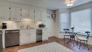 A modern kitchen with white cabinetry, a built-in microwave, and a dishwasher. There is a dining area with a table and chairs near a window with blinds. - Walking distance to the Augusta National and Surrey Center (Augusta)