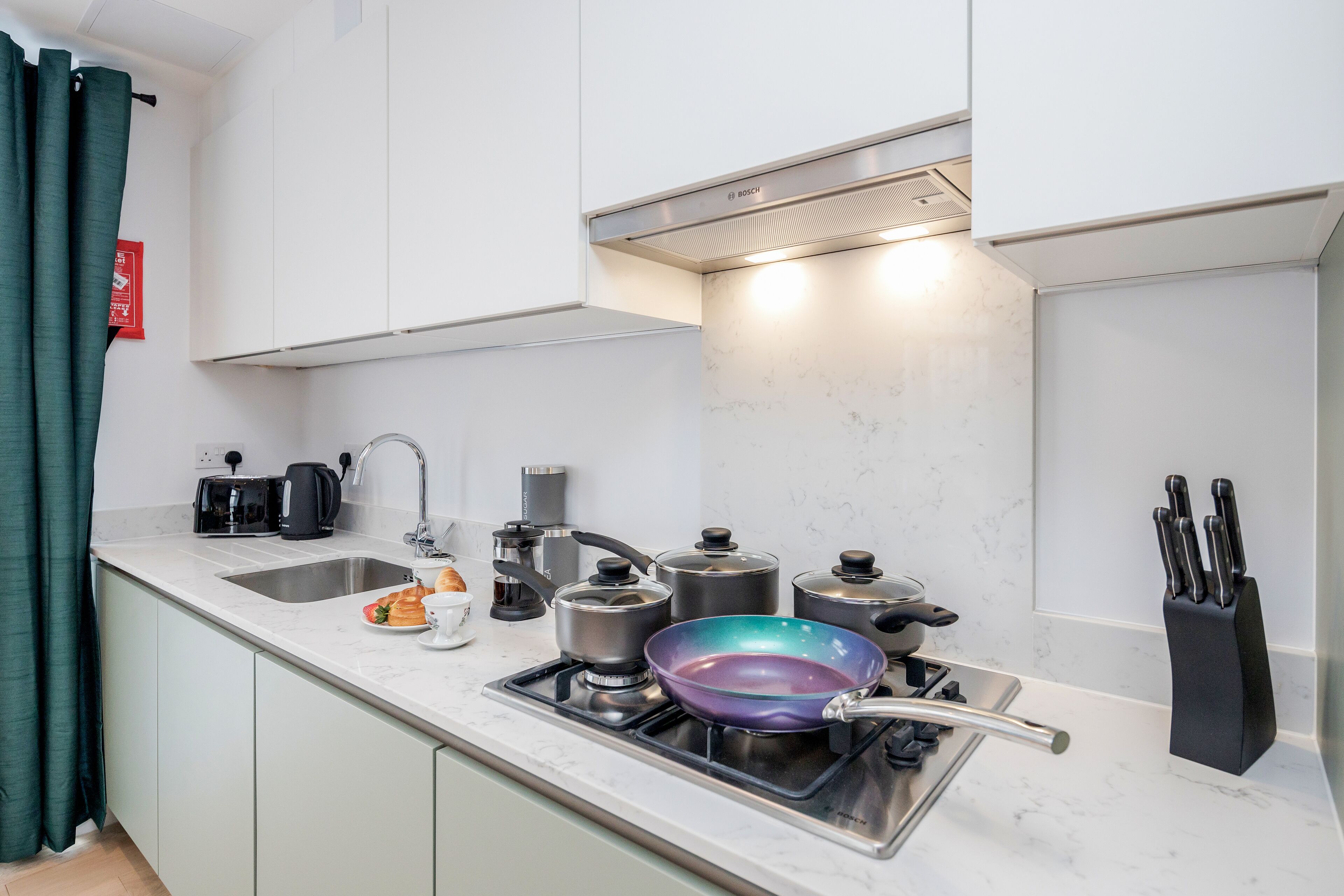 A modern kitchen with white cabinets, a stainless steel stove, and a variety of cooking utensils.