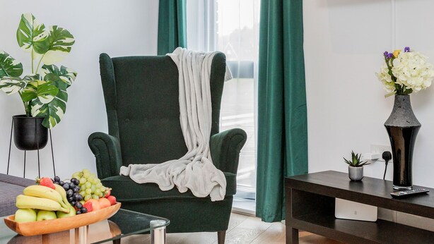 A modern living room with a green armchair, a glass coffee table, a fruit bowl, a potted plant, and a wall-mounted TV displaying "NETFLIX". - Watford Cassio Luxury - Modernview Serviced Accommodation (Watford)