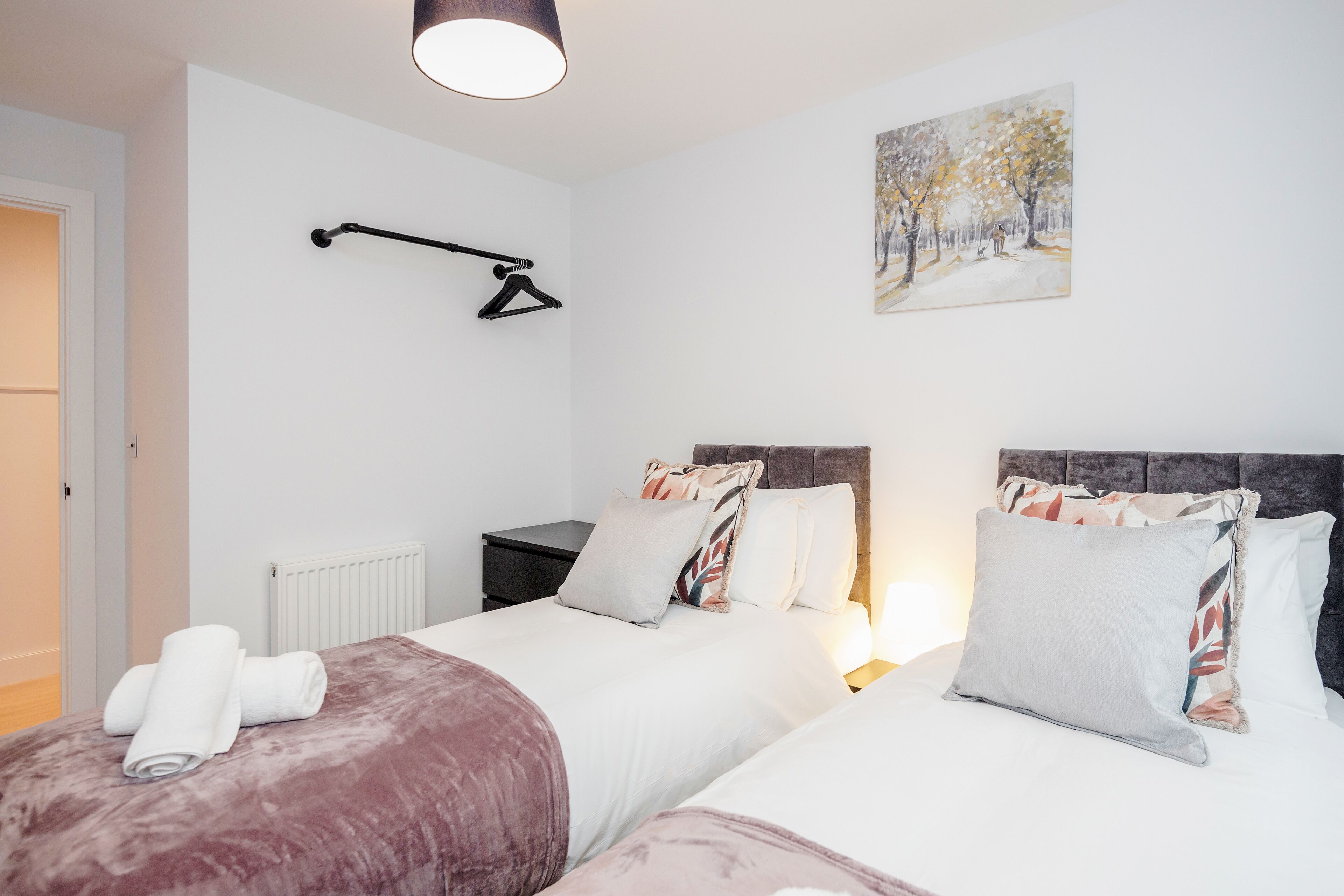 A hotel room with two beds, a radiator, a black hanger, and a painting of a snowy landscape.