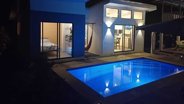 Een modern huis met een zwembad in de nacht, met grote ramen en een hangmat.
