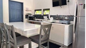 Een compacte keuken met een centraal kookeiland, een magnetron, een koffiezetapparaat en een koelkast.