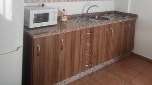 A kitchen with wooden cabinets, a white microwave, a sink, and a tiled backsplash. - Apartment routes of the torcal (Villanueva de la Concepción)