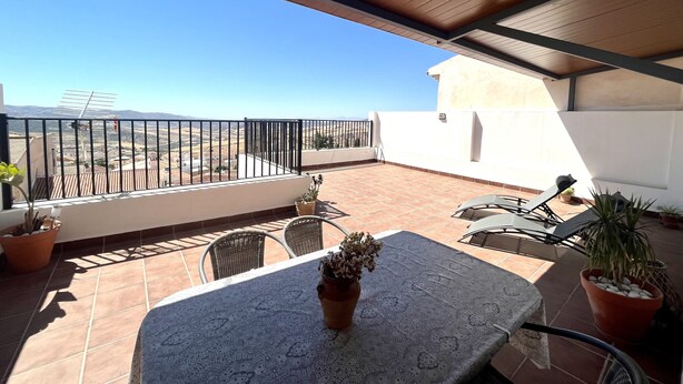 A covered patio with a table and chairs, potted plants, and a view of the countryside. - Apartment routes of the torcal (Villanueva de la Concepción)