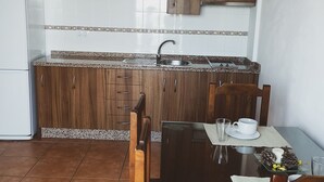 A compact kitchen with wooden cabinets, a white refrigerator, and a dining table with chairs. - Apartment routes of the torcal (Villanueva de la Concepción)