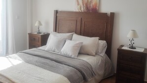 A neatly made bed with a wooden headboard, two bedside tables with lamps, and a painting above the headboard. - Apartment routes of the torcal (Villanueva de la Concepción)
