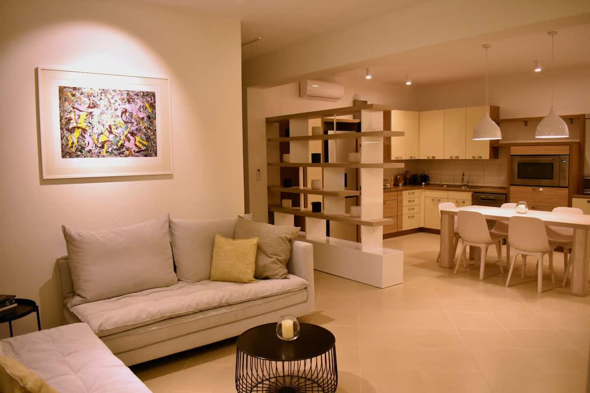 A modern living room with a sofa, a dining table with chairs, and a kitchen area with cabinets and appliances.