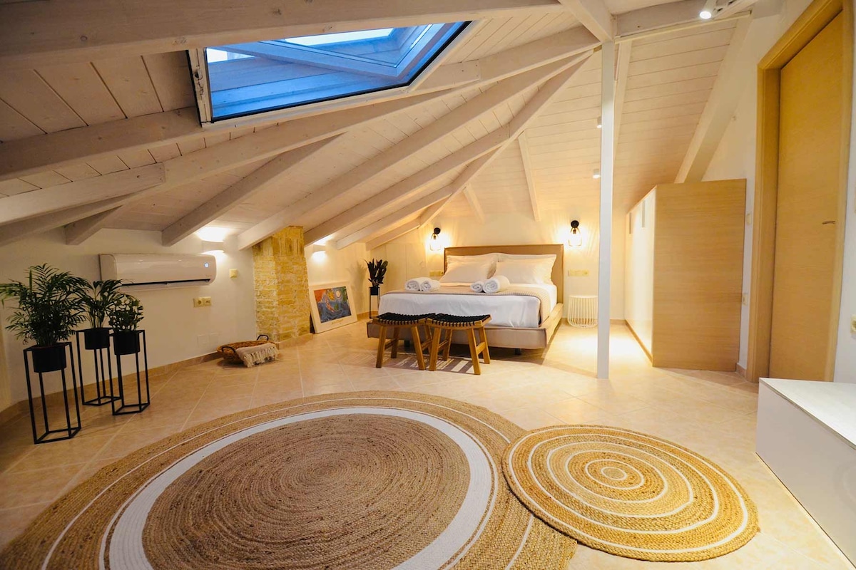 A bedroom with a skylight, a bed, a bedside table, a chair, and a rug.