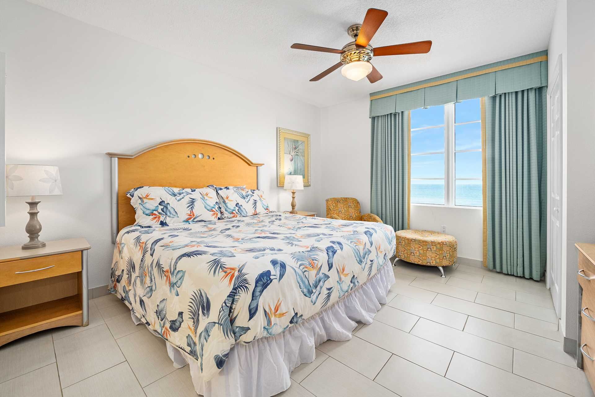 A bedroom with a bed, a ceiling fan, a window with curtains, and a chair.