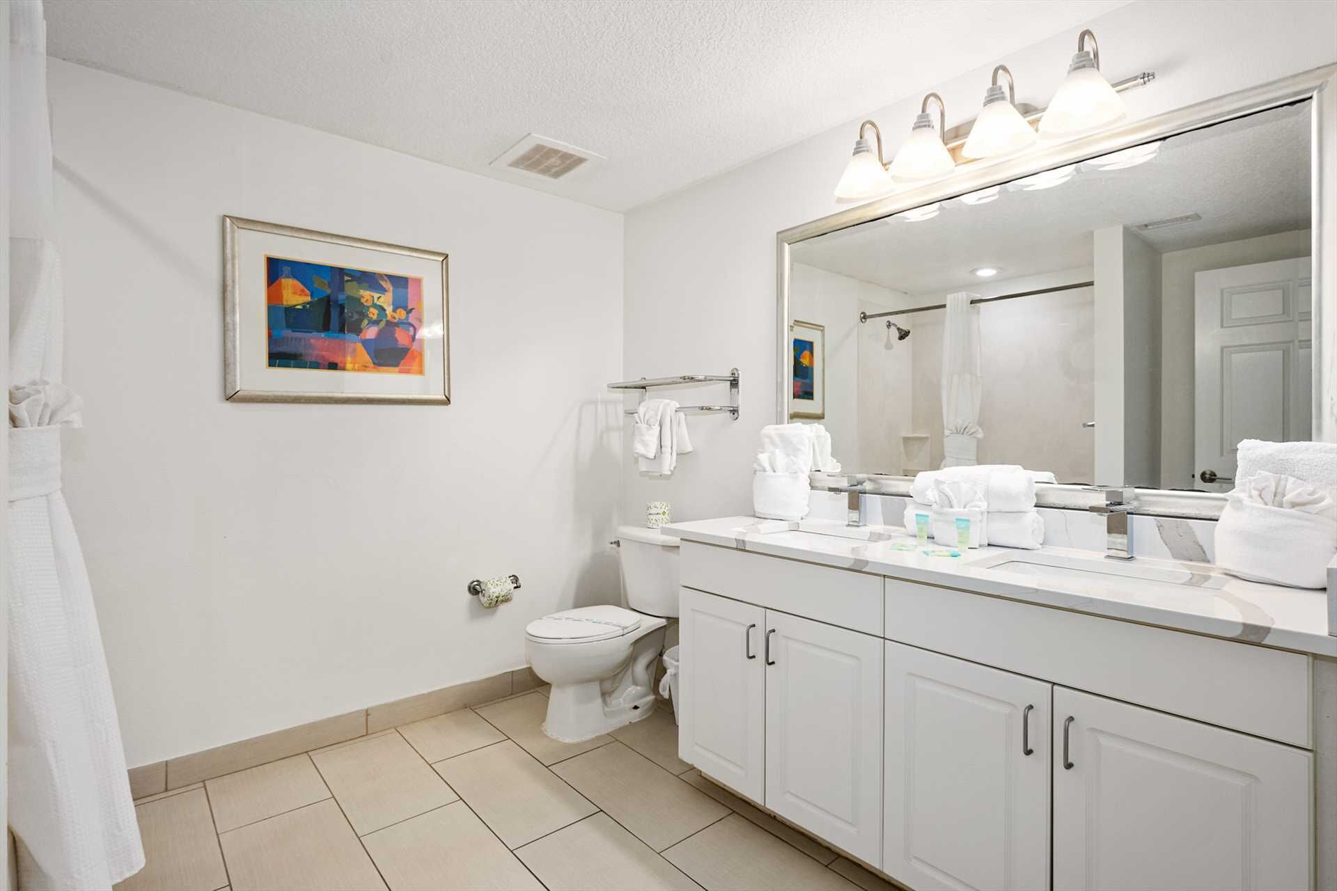 Une salle de bain moderne avec un lavabo blanc, un meuble-vasque et un grand miroir. On y trouve également des toilettes et un tableau encadré accroché au mur.