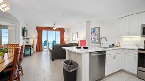 A modern kitchen with white cabinets, a dishwasher, and a dining area with a wooden table and chairs.