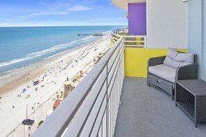 Un balcón con vista a la playa, un sofá de mimbre y un pilar morado.