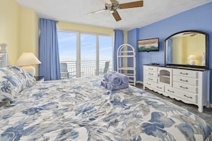 A bedroom with a bed, a dresser, a chair, a balcony, and a ceiling fan.