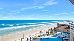 A beachfront hotel with a pool, beach access, and a pier in the background.