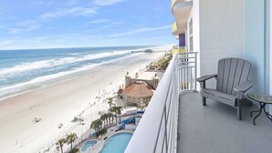 Een balkon met uitzicht op een strand en de oceaan, een zwembad en een stoel.