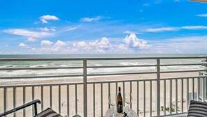 A balcony with a view of the beach and ocean, a bottle of wine, and a table with two glasses. - Luxury 12th Floor 2 BR Condo Direct Oceanfront Wyndham Ocean Walk Resort Daytona Beach | 1201 (Daytona Beach)