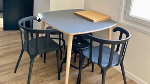 A modern dining area with a round table, four chairs, a flat-screen TV mounted on the wall, and a window providing natural light. - T3 5min from the beaches and creeks, FREE secure parking ! (La Ciotat)