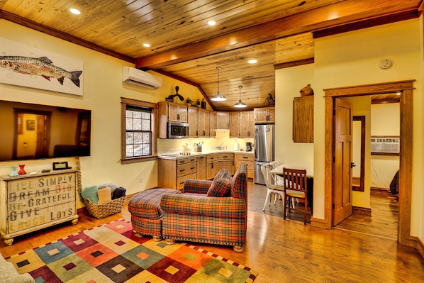 A cozy kitchen with wooden cabinets, a dining area with a plaid sofa, and a colorful rug.