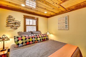 A bedroom with a wooden ceiling, a bed with a colorful quilt, a wall art piece, and a fish decoration.