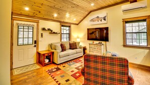 A cozy living room with a wooden ceiling, a sofa, a plaid chair, a rug, and a fish-themed artwork. - Want to REALLY get away? Round Bottom Roost. Secluded. Close to everything. (Mountain View)