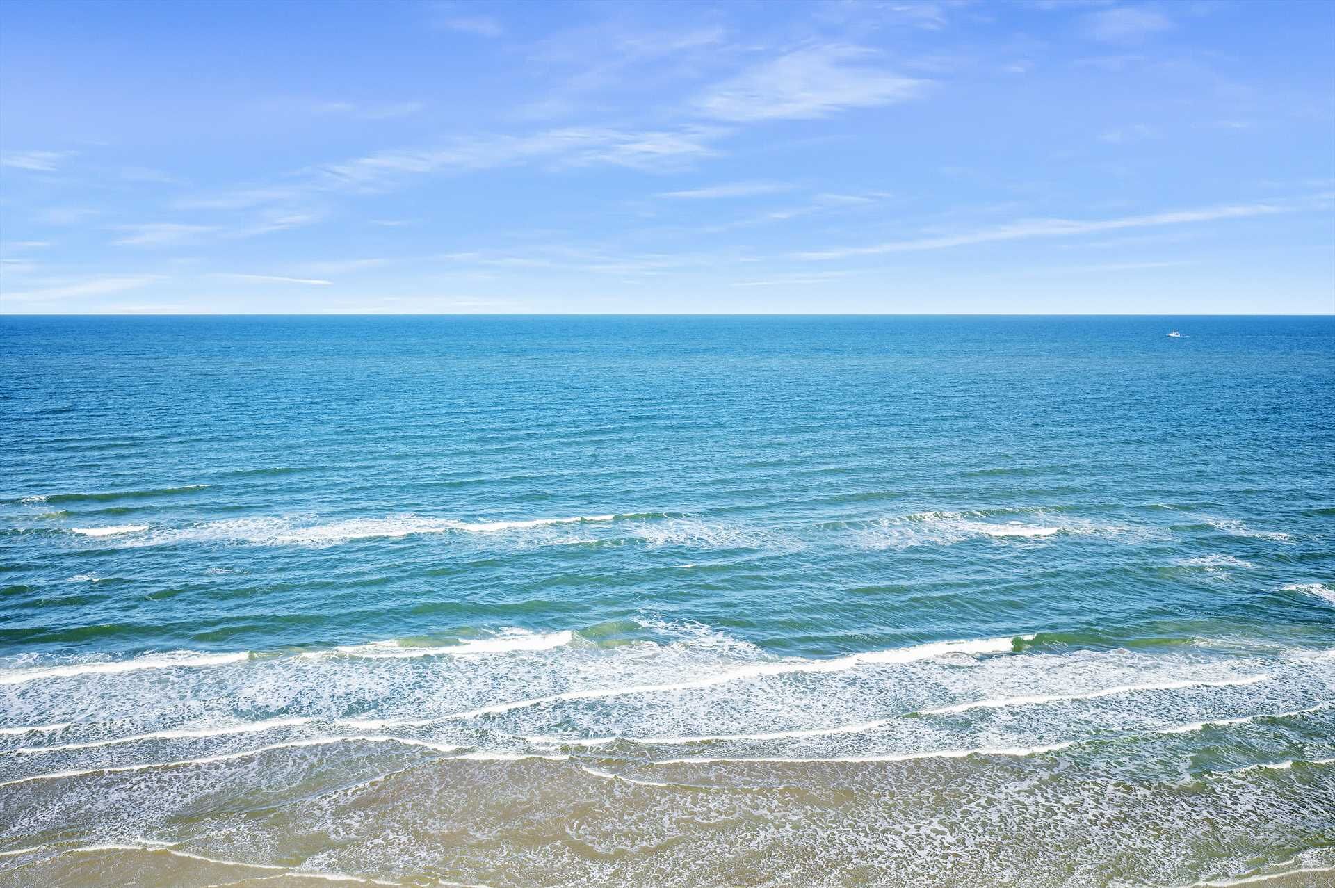 A beach with waves approaching the shore under a clear sky.