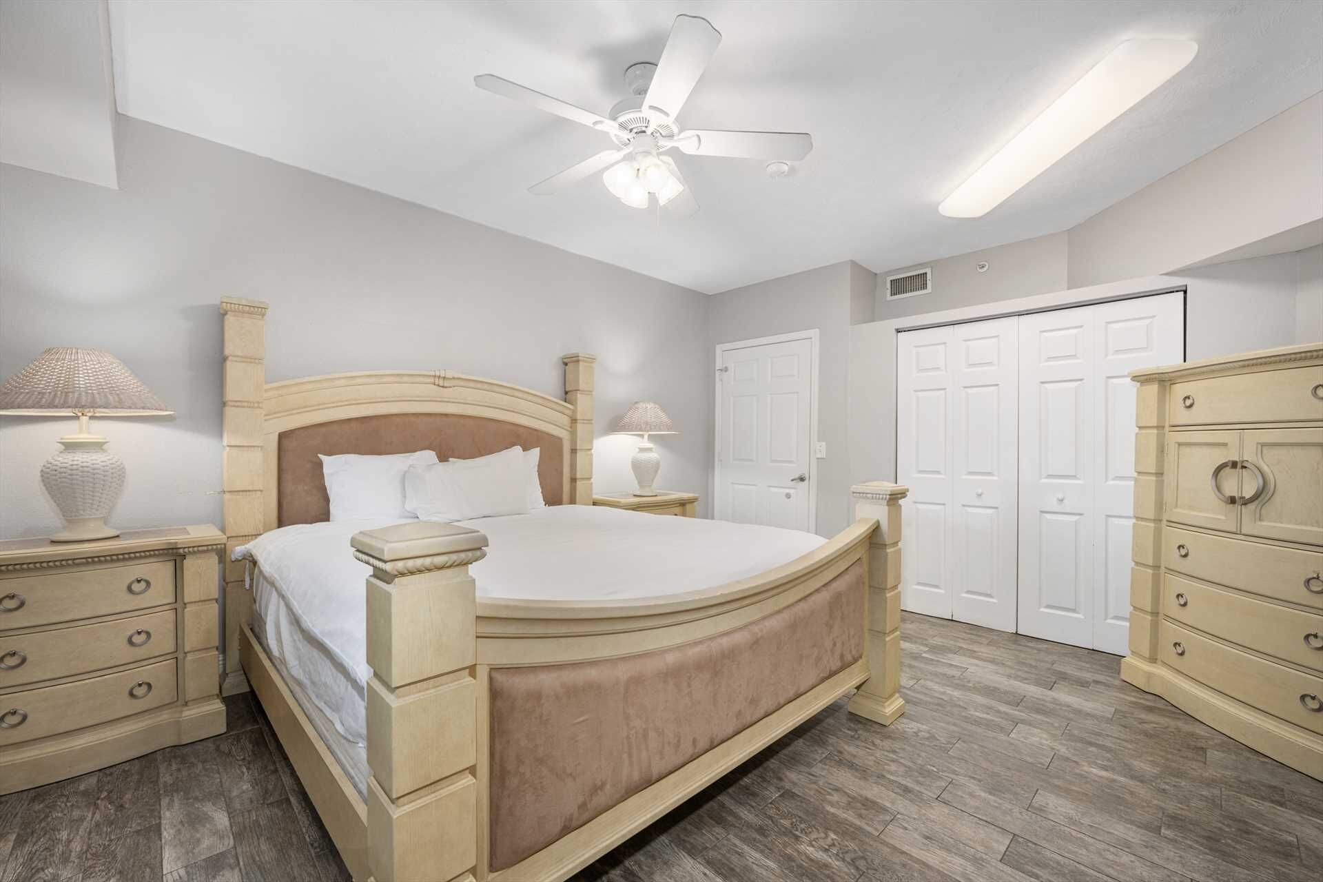 Un dormitorio con cama de madera, dos mesitas de noche con lámparas, un ventilador de techo y un armario.