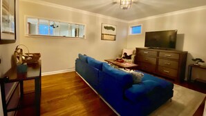 Ein Wohnzimmer mit einem blauen Sofa, Holzboden, einem Fernseher und einem kleinen Tisch.
