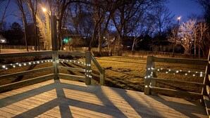 Eine Holzterrasse mit Lichterketten, umgeben von kahlen Bäumen und einer Rasenfläche.