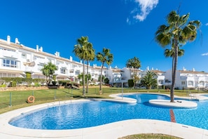 Une piscine bordée de palmiers, avec un bâtiment blanc en arrière-plan.