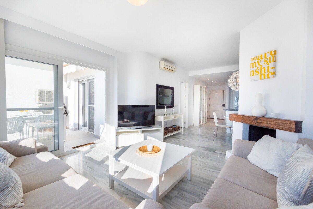 A modern living room with a flat-screen TV, a white coffee table, and a sofa.