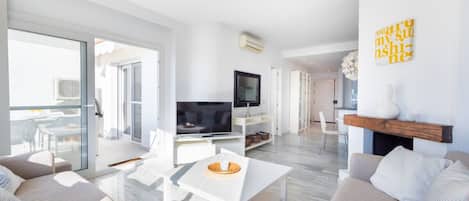 A modern living room with a flat-screen TV, a white coffee table, and a sofa.