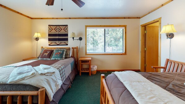 A cozy room with two beds, a window with blinds, a wooden headboard, a small table, and a lamp.