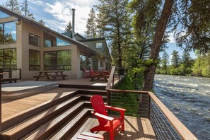 A wooden deck with a red Adirondack chair, a wooden table, and a bench.