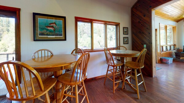 A dining area with a wooden table and chairs, large windows, and framed artwork on the walls. - 40-acre haven on the banks of the Fall River (Ashton)