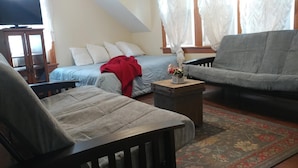 En hyggelig stue med en sofa, lænestol og en seng med et rødt tæppe.